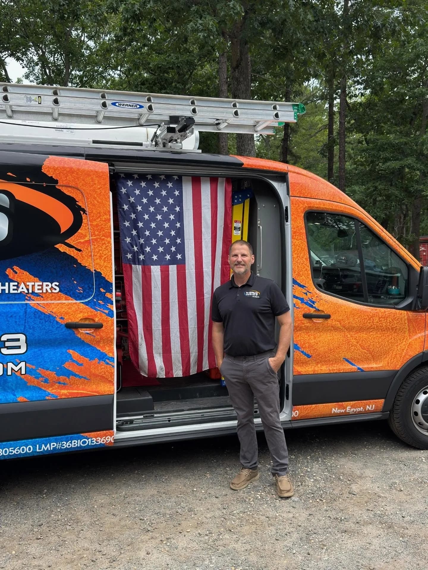 A technician from Dustin's stands beside an orange service van decorated with an American flag in New Egypt, NJ