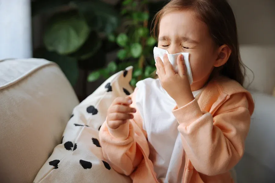 Young girl sneezing into a tissue at home, a sign poor indoor air quality may need Dustin's IAQ solutions in New Egypt, NJ
